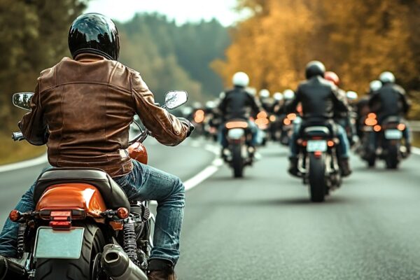 Biker wearing a brown leather jacket and helmet is riding his motorcycle on a country road, leading a group of bikers on a motorcycle trip