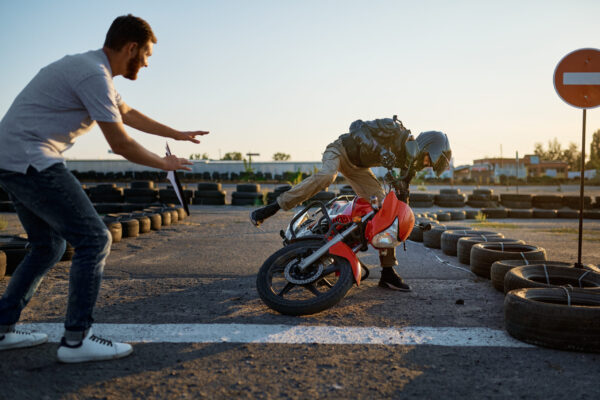 Male student in helmet falls off a motorbike, skill test on motordrome in motorcycle school. Training of motorcyclists beginners, biker practicing in motorschool