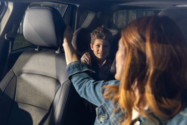 Woman looking back in car and talking to son in back seat, sharing a moment together during a daytime drive through the city