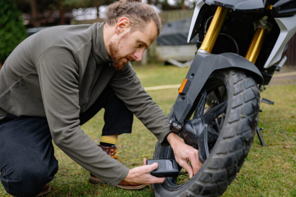 Man inflating front tire of ADV motorcycle with compact electric pump before trip.
