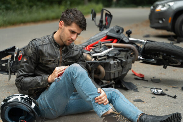 Motorcyclist sits on the asphalt near motorcycle, after road accidents with car. Broken and wrecked motorcycle on road